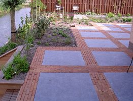 Terras van grote natuursteentegels afgewisseld met brede banen van gebakken klinkers.