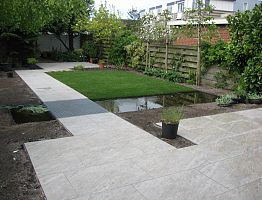 Vijver in de breedte van de tuin. Zicht vanaf het terras op het water.